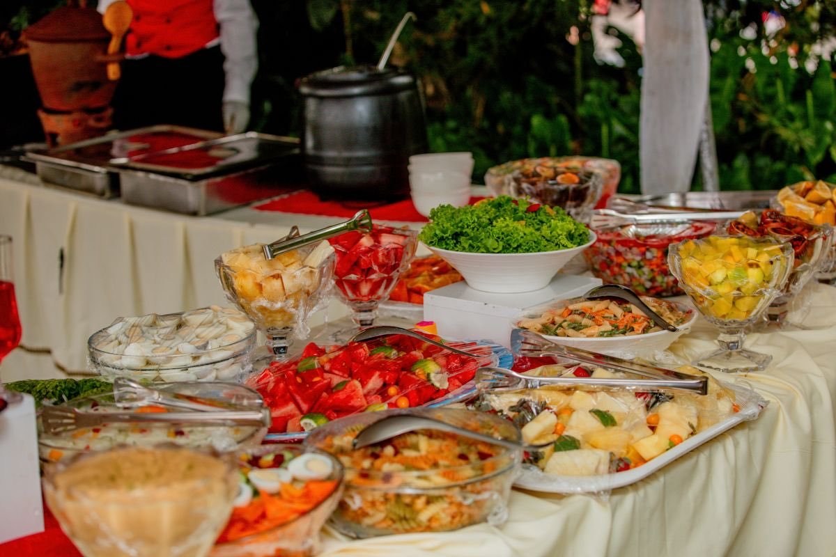 A buffet table with bowls of salads and fruit on a white tablecloth