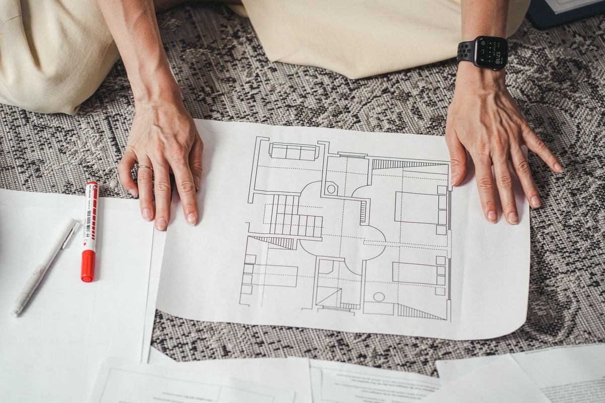 Hands resting on a printed floor plan laid out on the floor