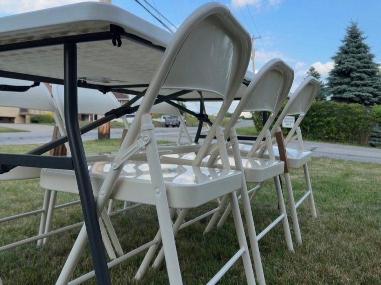 White folding chairs and a folding table set out on a lawn