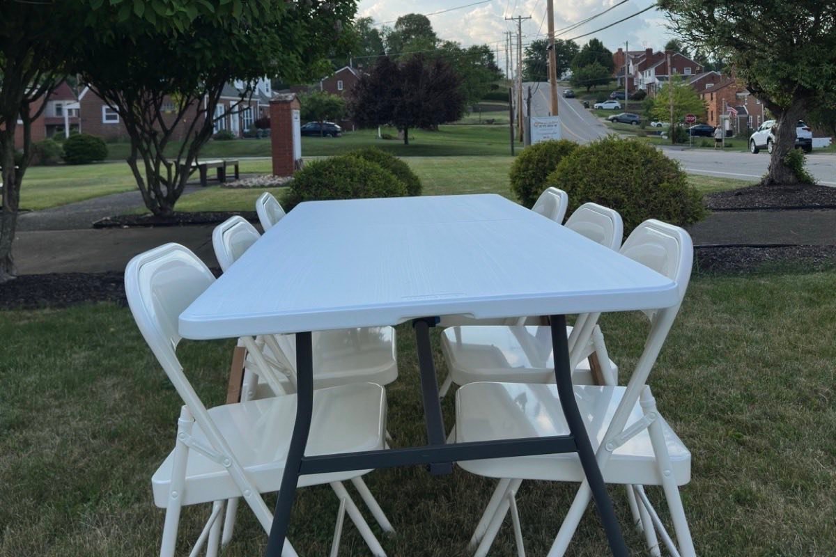 A folding table and white folding chairs set up on a lawn in front of a house